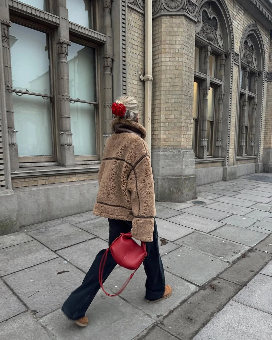 Tan textured jacket with dark flared trousers and red bag